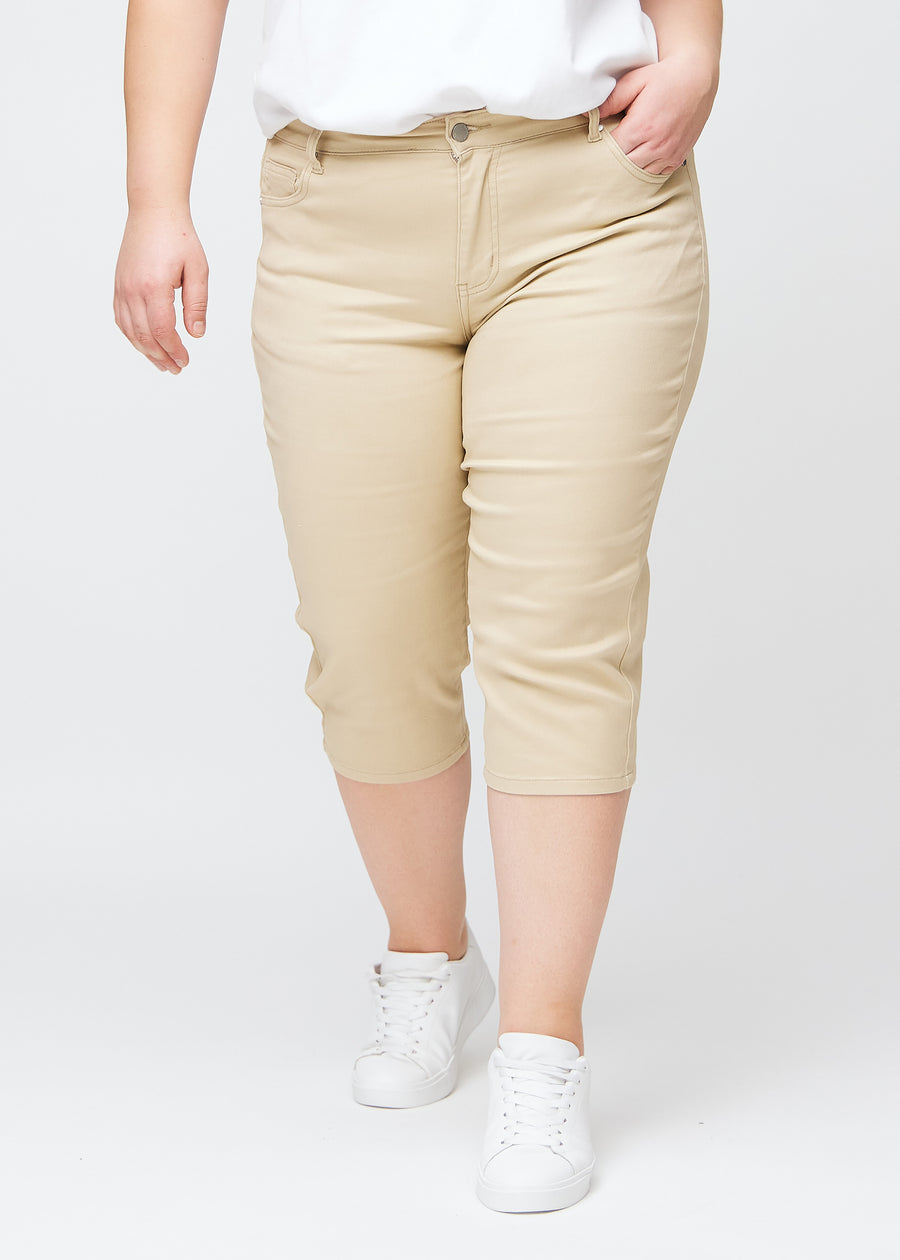 Slimcapris för kvinnor i beige jeanstyg, färgen Gazelles. Framifrån på en plus size-modell, med figursydd passform till strax under knät.