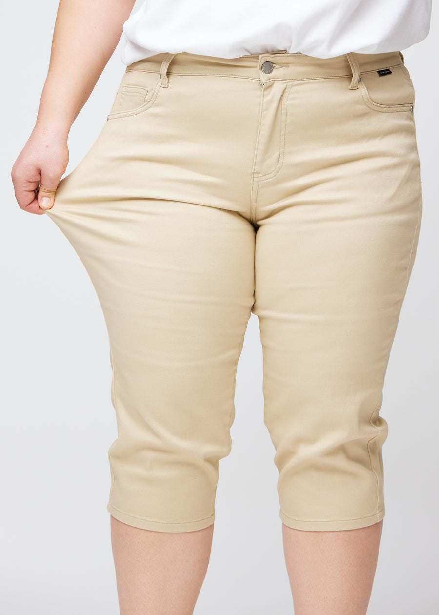 Slimcapris för kvinnor i beige jeanstyg, färgen Gazelles. En plus size-modell drar i tyget vid låret för att visa stretch och flexibilitet.