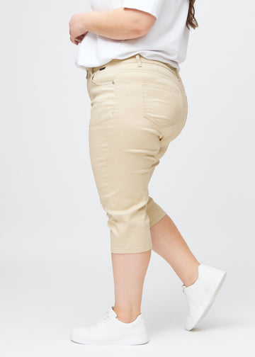 Slimcapris för kvinnor i beige jeanstyg, färgen Gazelles. Från sidan på en plus size-modell, med figursydd passform och medelhög midja (Mid Rise).