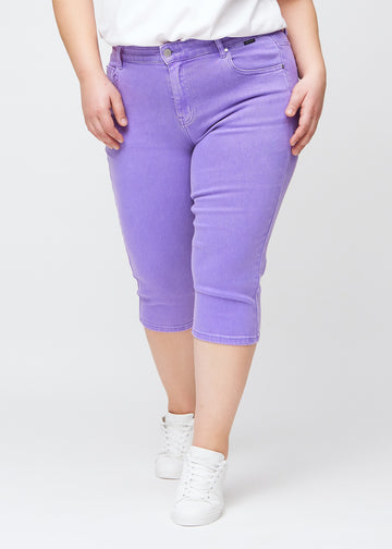 Slimcapris för kvinnor i pastellila jeanstyg, färgen Lavenders. Framifrån på en plus size-modell, med figursydd passform till strax under knät.