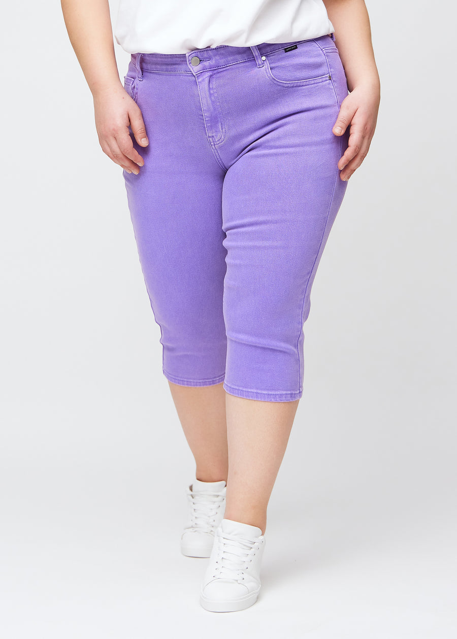 Slimcapris för kvinnor i pastellila jeanstyg, färgen Lavenders. Framifrån på en plus size-modell, med figursydd passform till strax under knät.