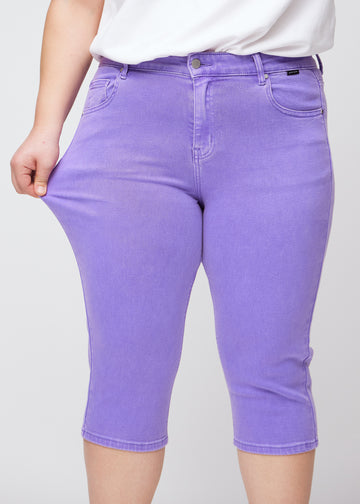 Slimcapris för kvinnor i pastellila jeanstyg, färgen Lavenders. En plus size-modell drar i tyget vid låret för att visa stretch och flexibilitet.