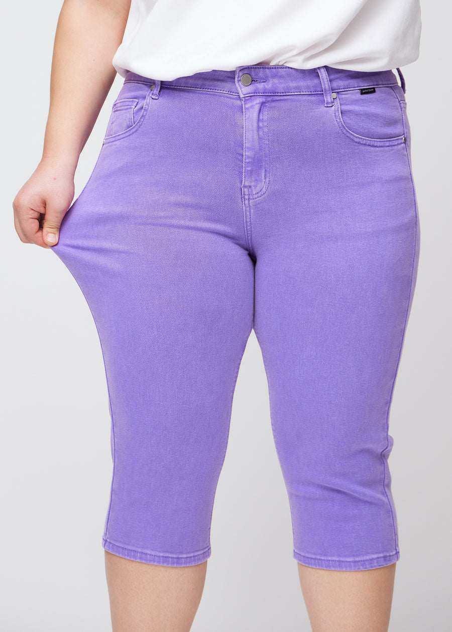 Slimcapris för kvinnor i pastellila jeanstyg, färgen Lavenders. En plus size-modell drar i tyget vid låret för att visa stretch och flexibilitet.