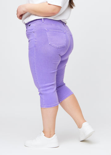 Slimcapris för kvinnor i pastellila jeanstyg, färgen Lavenders. Från sidan på en plus size-modell, med figursydd passform och medelhög midja (Mid Rise).