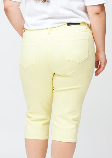 Slimcapris för kvinnor i pastellljusgult jeanstyg, färgen Lemonades. Närbild bakifrån på en plus size-modell, med fokus på bakfickor och sömmar.