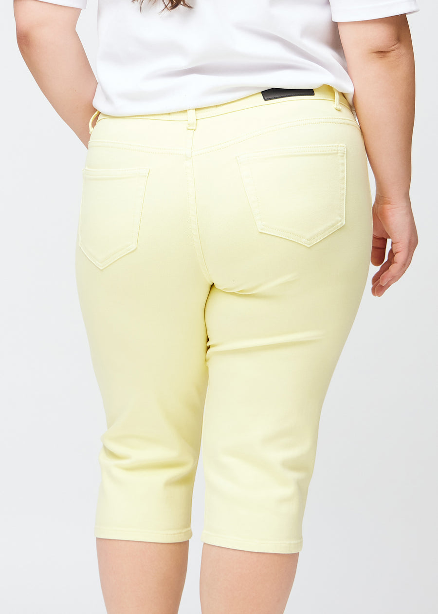 Slimcapris för kvinnor i pastellljusgult jeanstyg, färgen Lemonades. Närbild bakifrån på en plus size-modell, med fokus på bakfickor och sömmar.