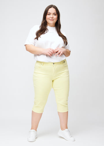Slimcapris för kvinnor i pastellljusgult jeanstyg, färgen Lemonades. Helbild av en plus size-modell som bär slimcapris.