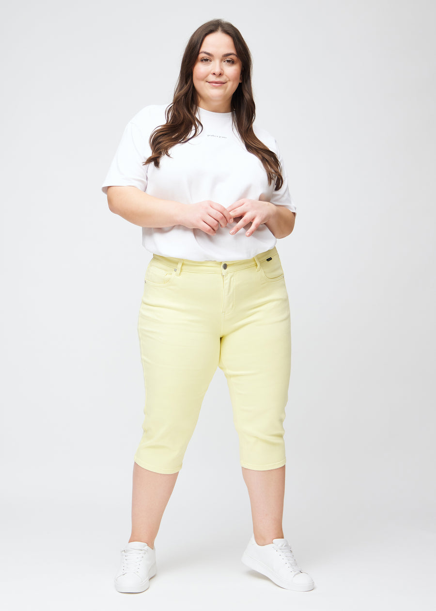 Slimcapris för kvinnor i pastellljusgult jeanstyg, färgen Lemonades. Helbild av en plus size-modell som bär slimcapris.