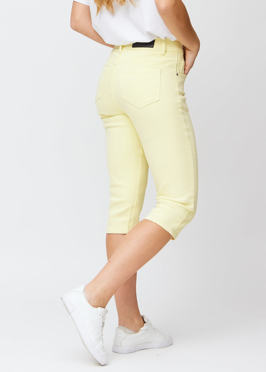 Slimcapris för kvinnor i pastellljusgult jeanstyg, färgen Lemonades. Bakifrån på en modell, med fokus på passform, längd och bakfickor.