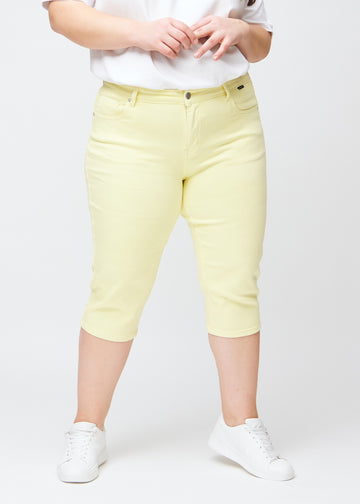 Slimcapris för kvinnor i pastellljusgult jeanstyg, färgen Lemonades. Framifrån på en plus size-modell, med figursydd passform till strax under knät.