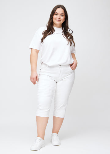 Slimcapris för kvinnor i vitt jeanstyg, färgen Marguerites. Helbild av en plus size-modell som bär slimcapris.