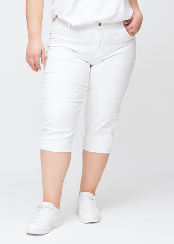 Slimcapris för kvinnor i vitt jeanstyg, färgen Marguerites. Framifrån på en plus size-modell, med figursydd passform till strax under knät.