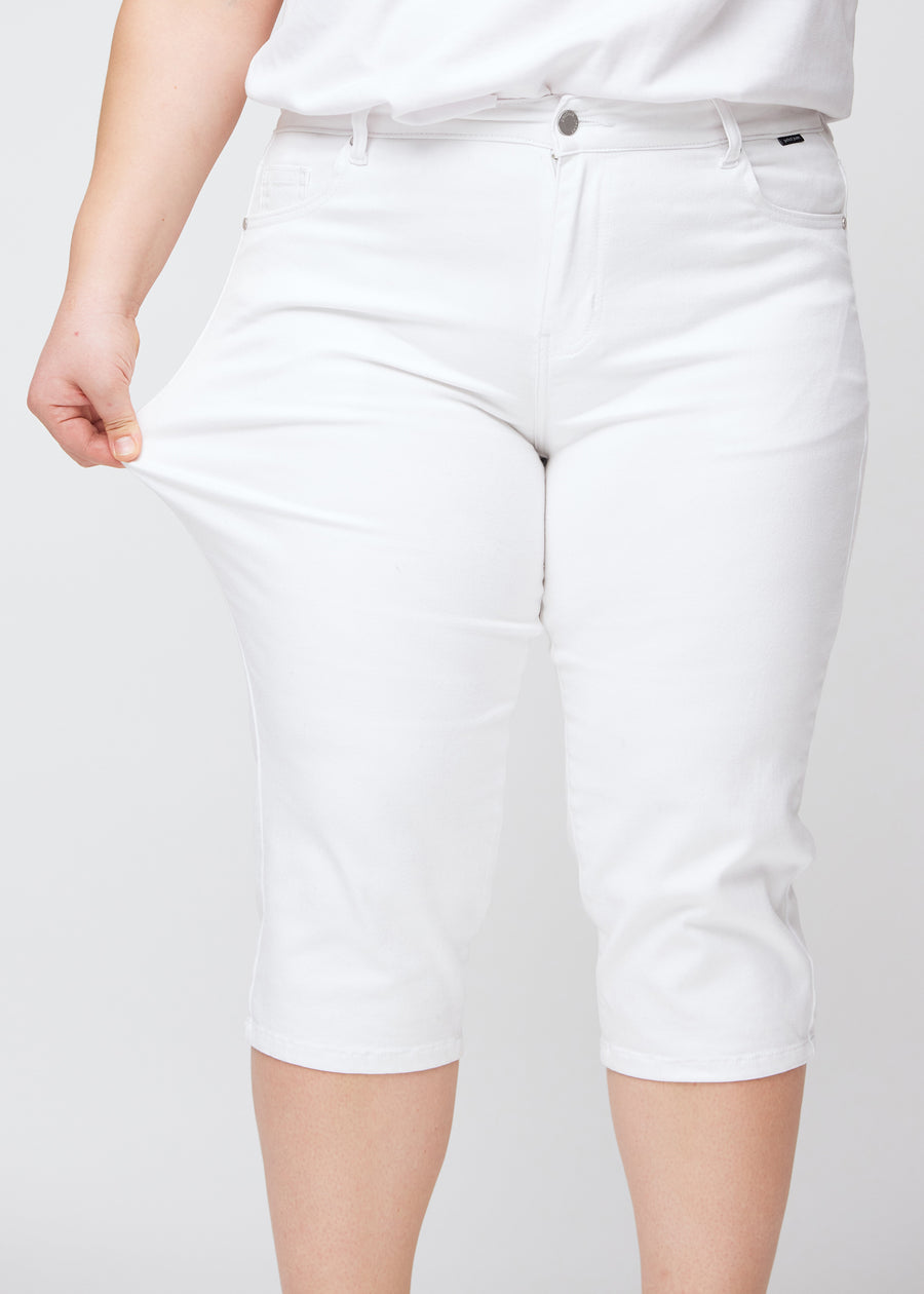 Slimcapris för kvinnor i vitt jeanstyg, färgen Marguerites. En plus size-modell drar i tyget vid låret för att visa stretch och flexibilitet.