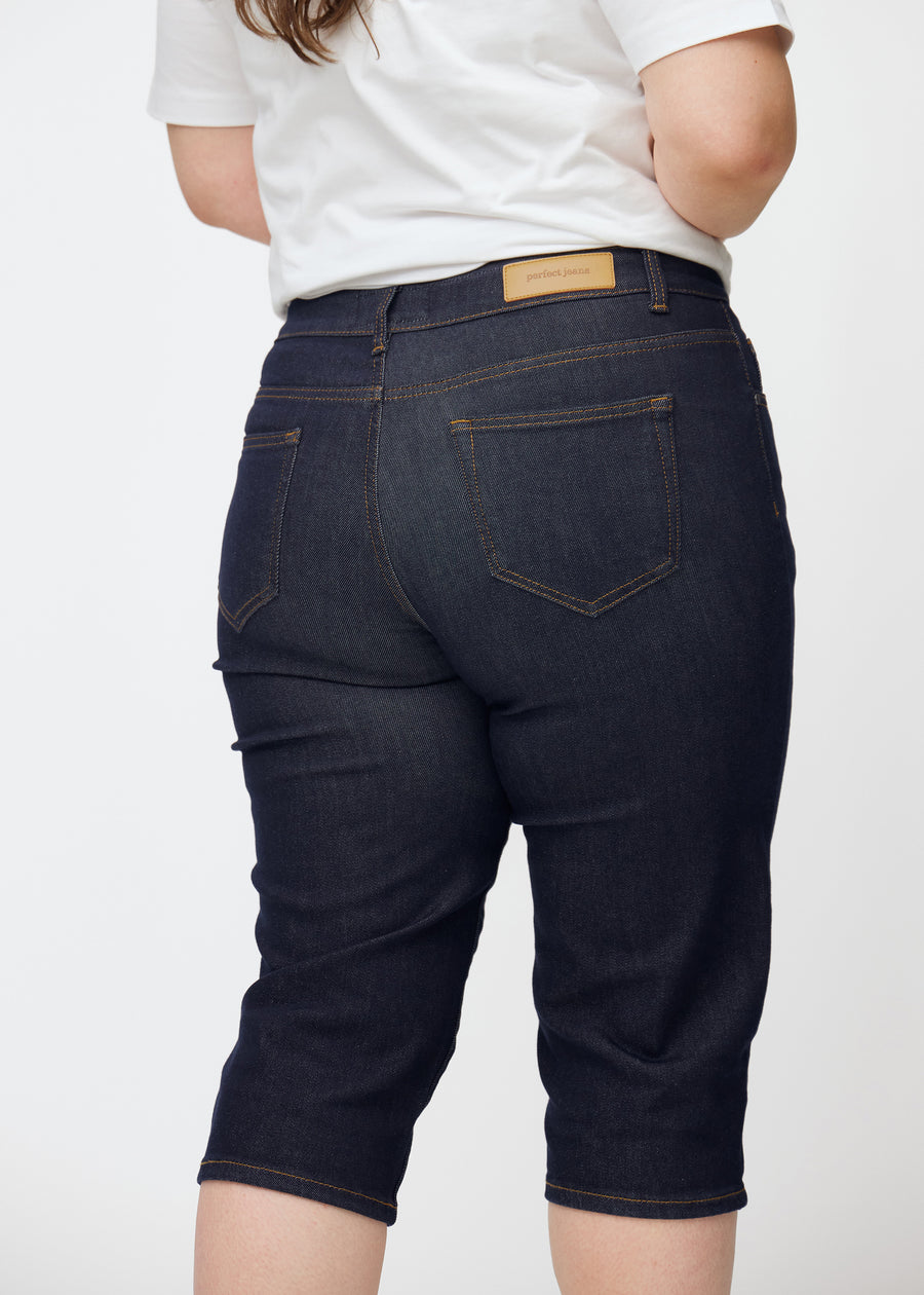 Mörkblå denim capris för dam i färgen Midnights sett bakifrån i närbild på plus-size modell.