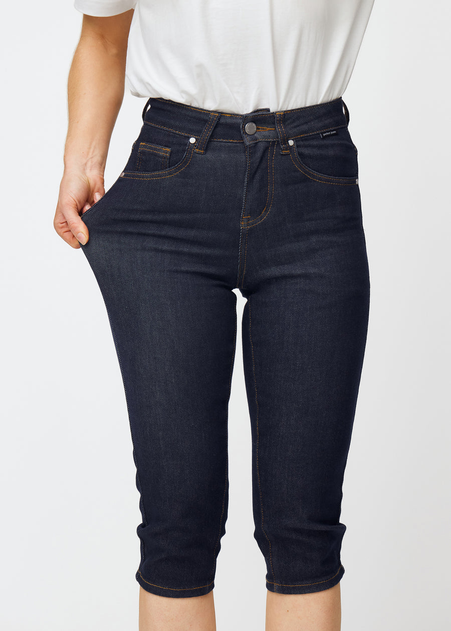 Modell sträcker mörkblå denim capris för dam i färgen Midnights vid låret för att visa materialets stretch.