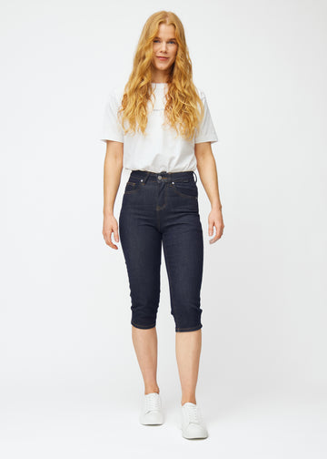 Helbild av modell i mörkblå denim capris för dam i färgen Midnights med slim passform.