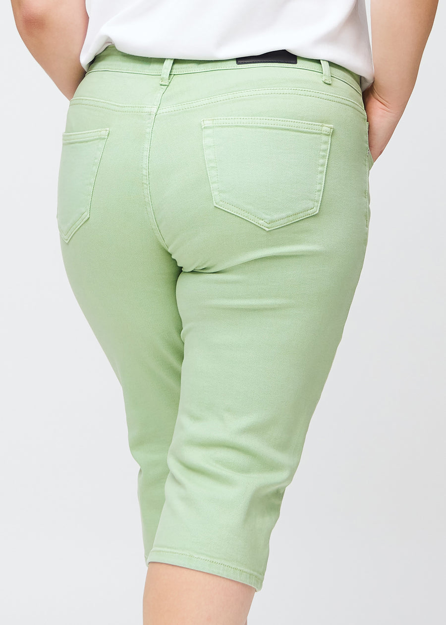 Slimcapris för kvinnor i pastellljusgrönt jeanstyg, färgen Mints. Närbild bakifrån på en plus size-modell, med fokus på bakfickor och sömmar.