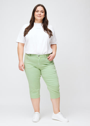 Slimcapris för kvinnor i pastellljusgrönt jeanstyg, färgen Mints. Helbild av en plus size-modell som bär slimcapris.