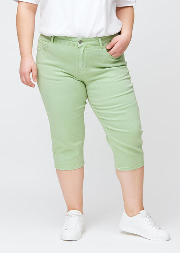 Slimcapris för kvinnor i pastellljusgrönt jeanstyg, färgen Mints. Framifrån på en plus size-modell, med figursydd passform till strax under knät.