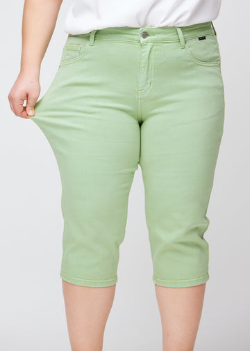 Slimcapris för kvinnor i pastellljusgrönt jeanstyg, färgen Mints. En plus size-modell drar i tyget vid låret för att visa stretch och flexibilitet.