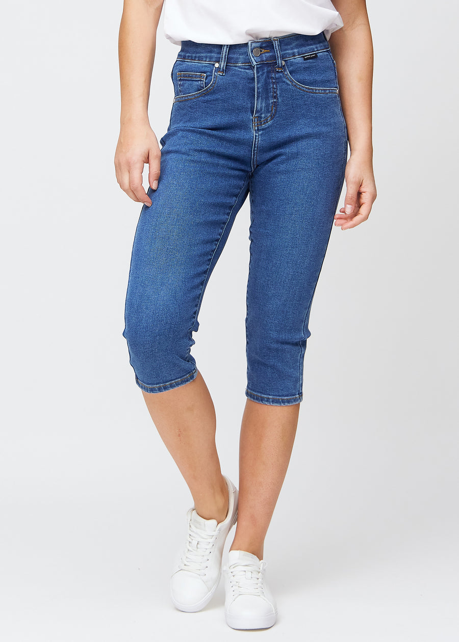 Slimcapris för kvinnor i mörkblå denim, färgen Oceans. Framifrån på en modell, med figursydd passform till strax under knät.