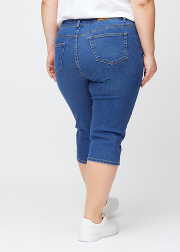 Slimcapris för kvinnor i mörkblå denim, färgen Oceans. Bakifrån på en plus size-modell, med fokus på passform, längd och bakfickor.