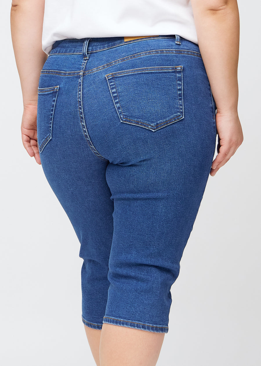 Slimcapris för kvinnor i mörkblå denim, färgen Oceans. Närbild bakifrån på en plus size-modell, med fokus på bakfickor och sömmar.