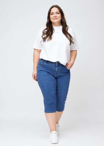 Slimcapris för kvinnor i mörkblå denim, färgen Oceans. Helbild av en plus size-modell som bär slimcapris.