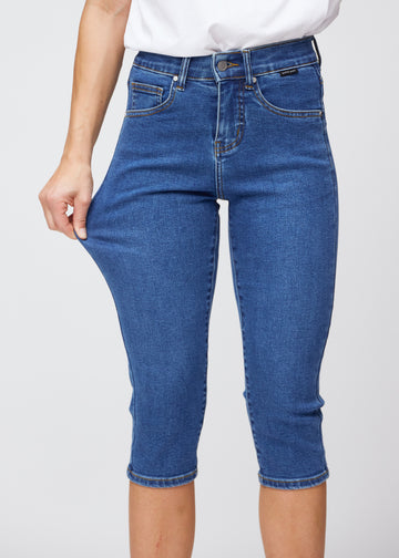 Slimcapris för kvinnor i mörkblå denim, färgen Oceans. En modell drar i tyget vid låret för att visa stretch och flexibilitet.