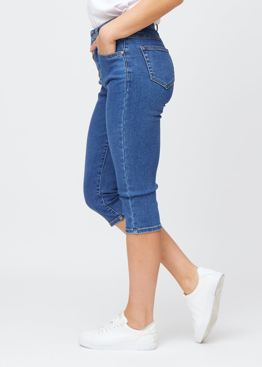 Slimcapris för kvinnor i mörkblå denim, färgen Oceans. Från sidan på en modell, med figursydd passform och medelhög midja (Mid Rise).