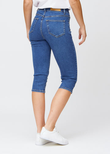 Slimcapris för kvinnor i mörkblå denim, färgen Oceans. Bakifrån på en modell, med fokus på passform, längd och bakfickor.