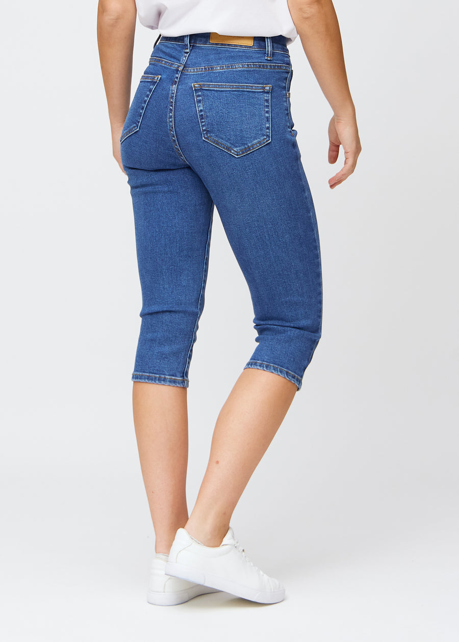 Slimcapris för kvinnor i mörkblå denim, färgen Oceans. Bakifrån på en modell, med fokus på passform, längd och bakfickor.