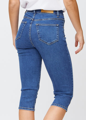 Slimcapris för kvinnor i mörkblå denim, färgen Oceans. Närbild bakifrån på en modell, med fokus på bakfickor och sömmar.
