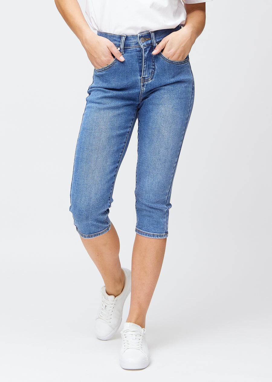 Slimcapris för kvinnor i blå denim, färgen Rivers. Framifrån på en modell, med figursydd passform till strax under knät.