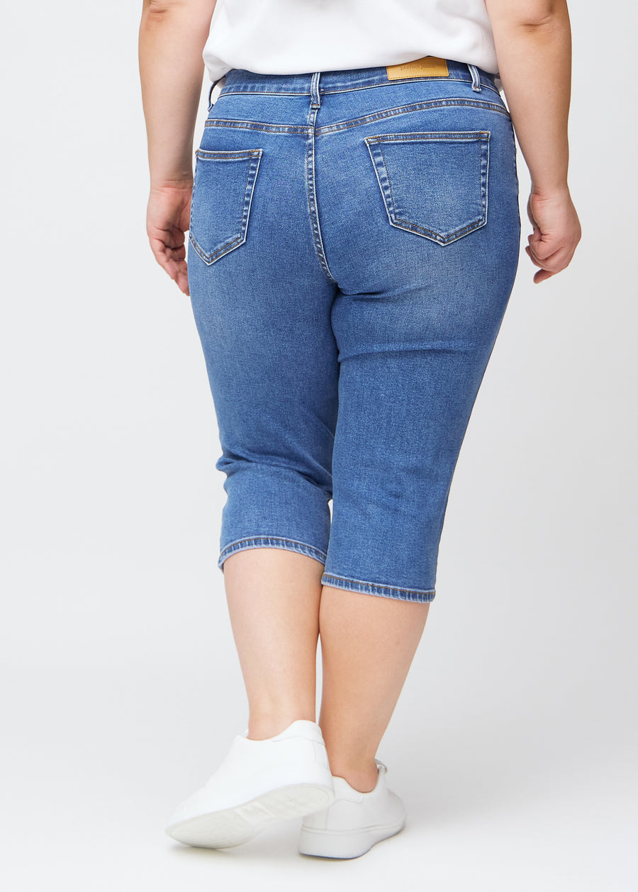Slimcapris för kvinnor i blå denim, färgen Rivers. Bakifrån på en plus size-modell, med fokus på passform, längd och bakfickor.