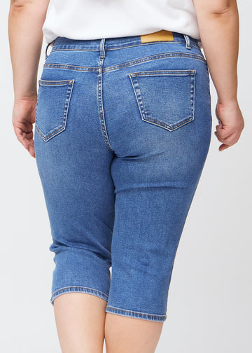 Slimcapris för kvinnor i blå denim, färgen Rivers. Närbild bakifrån på en plus size-modell, med fokus på bakfickor och sömmar.