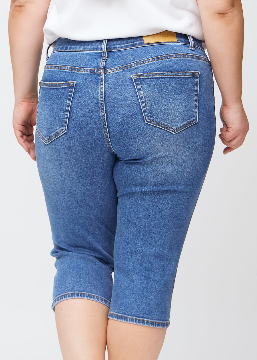 Slimcapris för kvinnor i blå denim, färgen Rivers. Närbild bakifrån på en plus size-modell, med fokus på bakfickor och sömmar.