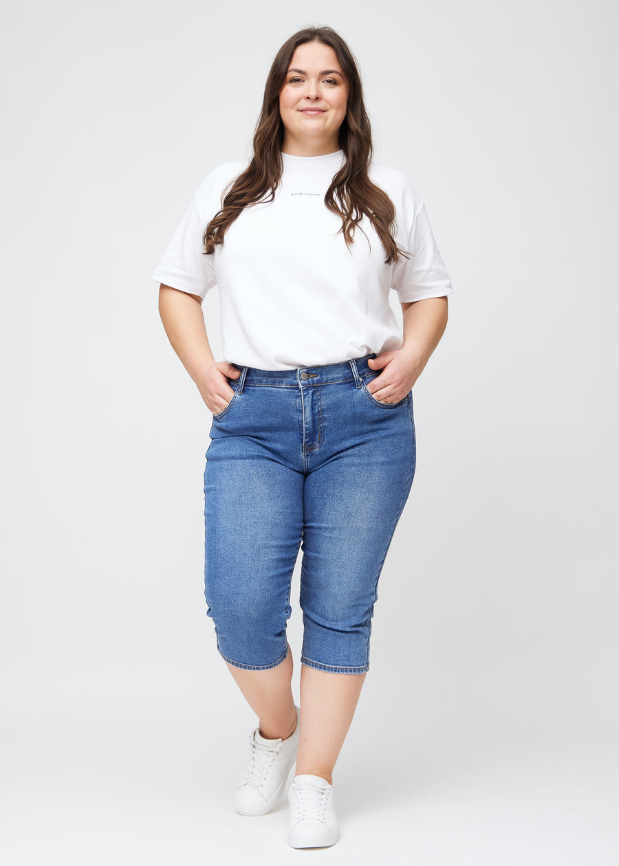 Slimcapris för kvinnor i blå denim, färgen Rivers. Helbild av en plus size-modell som bär slimcapris.