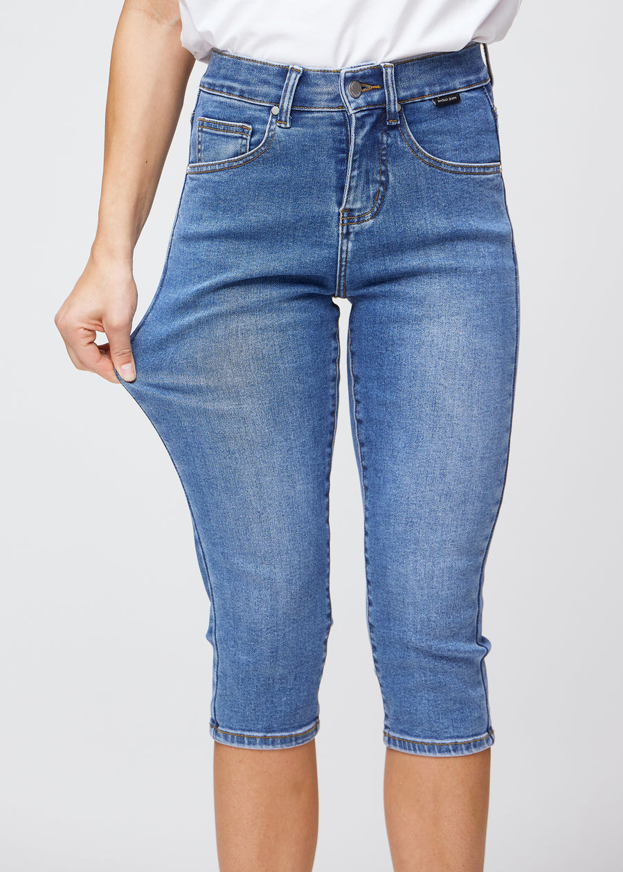 Slimcapris för kvinnor i blå denim, färgen Rivers. En modell drar i tyget vid låret för att visa stretch och flexibilitet.