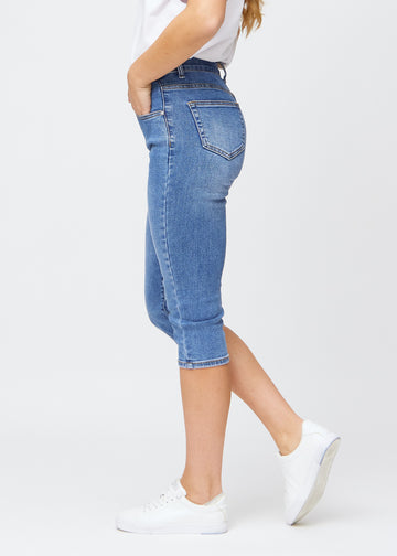 Slimcapris för kvinnor i blå denim, färgen Rivers. Från sidan på en modell, med figursydd passform och medelhög midja (Mid Rise).