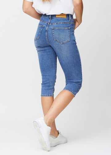 Slimcapris för kvinnor i blå denim, färgen Rivers. Bakifrån på en modell, med fokus på passform, längd och bakfickor.