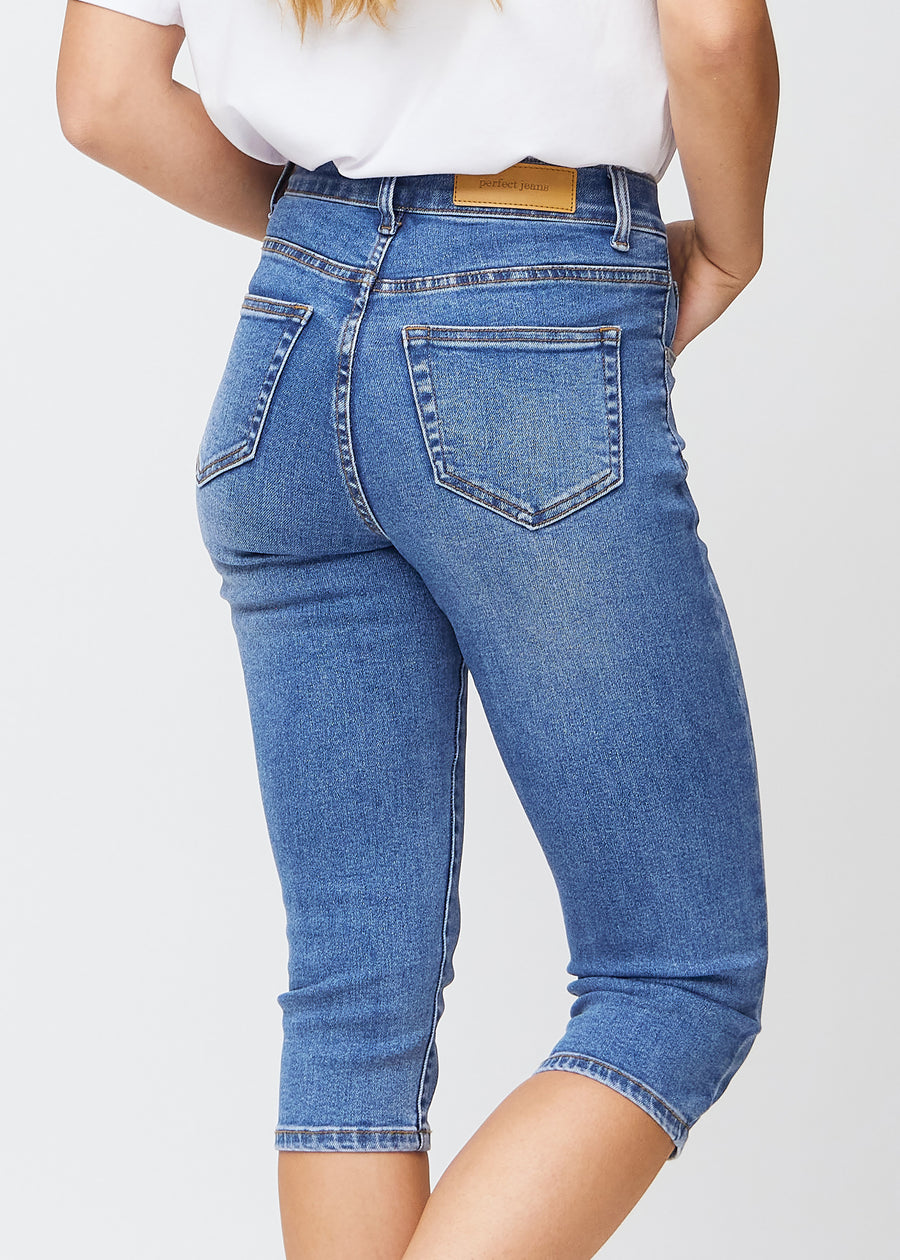 Slimcapris för kvinnor i blå denim, färgen Rivers. Närbild bakifrån på en modell, med fokus på bakfickor och sömmar.