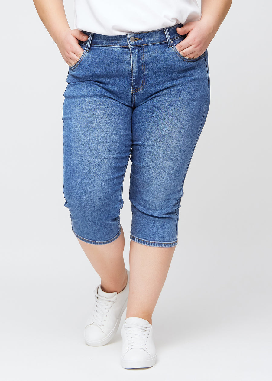 Slimcapris för kvinnor i blå denim, färgen Rivers. Framifrån på en plus size-modell, med figursydd passform till strax under knät.
