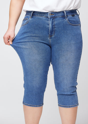 Slimcapris för kvinnor i blå denim, färgen Rivers. En plus size-modell drar i tyget vid låret för att visa stretch och flexibilitet.