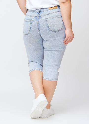 Slimcapris för kvinnor i ljusblå denim, färgen Waves. Bakifrån på en plus size-modell, med fokus på passform, längd och bakfickor.