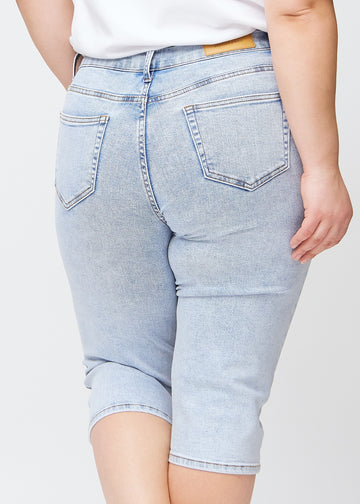 Slimcapris för kvinnor i ljusblå denim, färgen Waves. Närbild bakifrån på en plus size-modell, med fokus på bakfickor och sömmar.