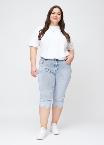 Slimcapris för kvinnor i ljusblå denim, färgen Waves. Helbild av en plus size-modell som bär slimcapris.