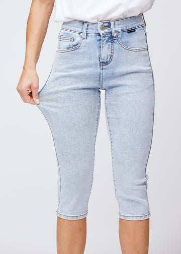 Slimcapris för kvinnor i ljusblå denim, färgen Waves. En modell drar i tyget vid låret för att visa stretch och flexibilitet.
