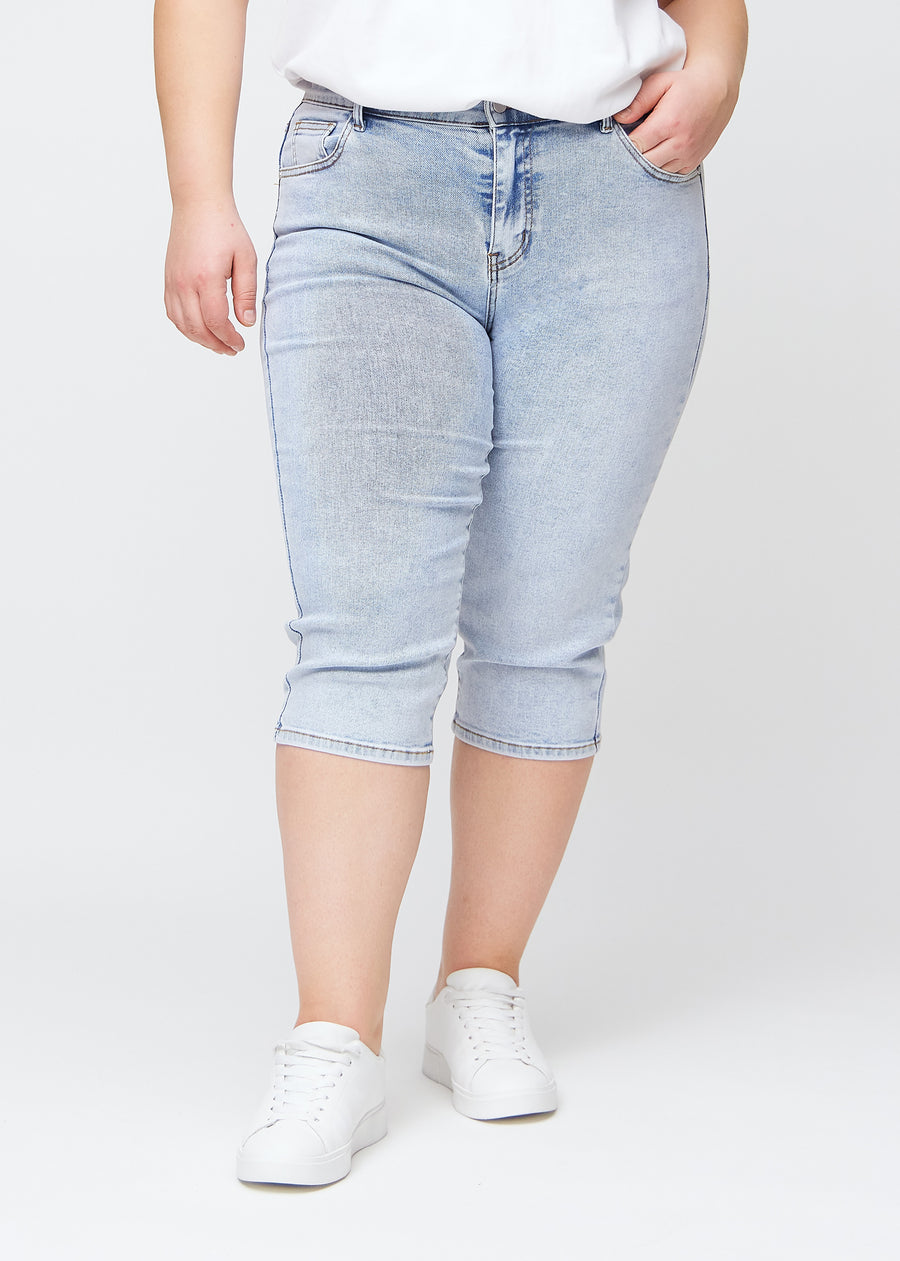 Slimcapris för kvinnor i ljusblå denim, färgen Waves. Framifrån på en plus size-modell, med figursydd passform till strax under knät.