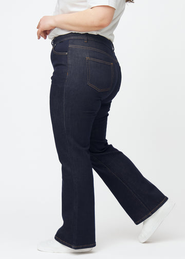 Djupt mörkblå denim jeans för kvinnor i färgen Midnights med bootcut-passform sedd från sidan på plus size-modell.